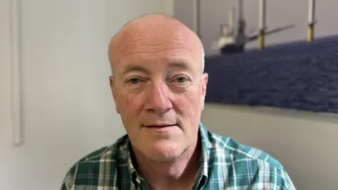 BBC News A grey haired man in a green shirt looking into the camera 