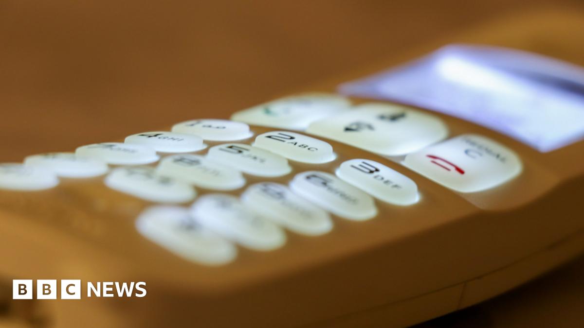A white man with brown hair standing outside a house in the rural countryside smiling.