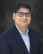 headshot of Anurag Chaturvedi, a man wearing glasses and a dark suit in front of a dark background