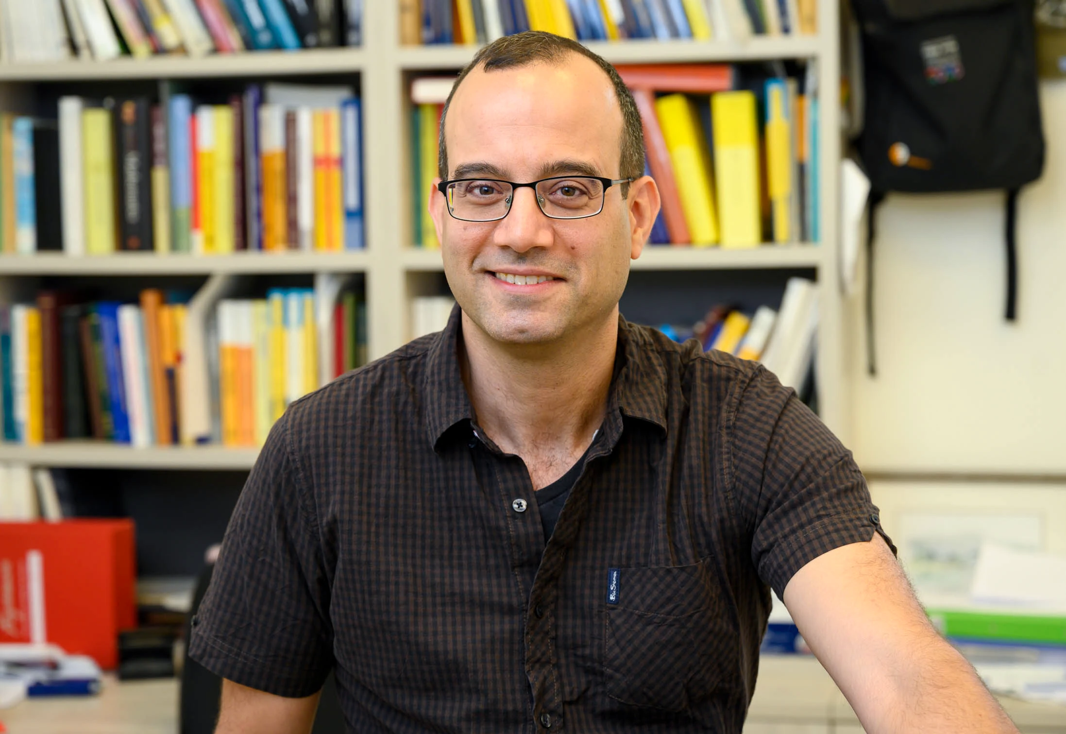 Man in glasses smiling in front of bookshelf.