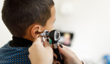 a close up of a doctor's hands using an otoscope to examine a young boy's ear