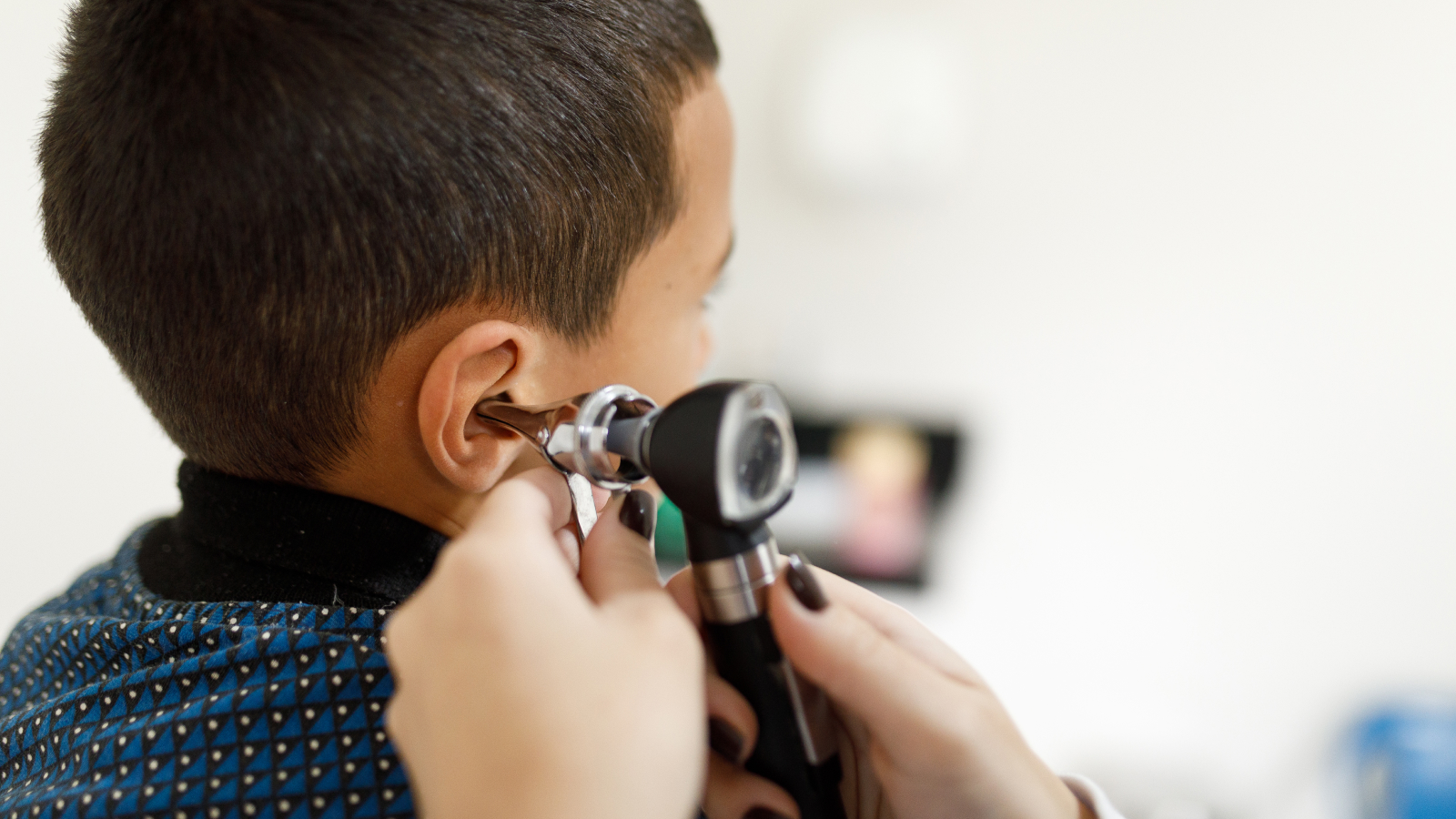 a close up of a doctor's hands using an otoscope to examine a young boy's ear