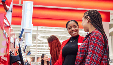 A person stands at a Target store checkout. They are wearing a team member name badge and are smiling at another person.
