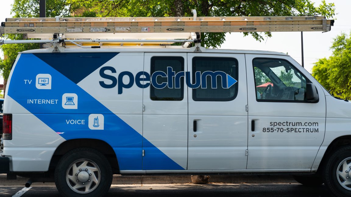 A parked van used by a Spectrum cable technician. The van has the Spectrum logo on its side and a ladder stowed on the roof.