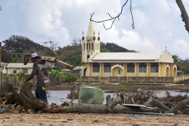 photo of a man clearing debris with a church in the background.