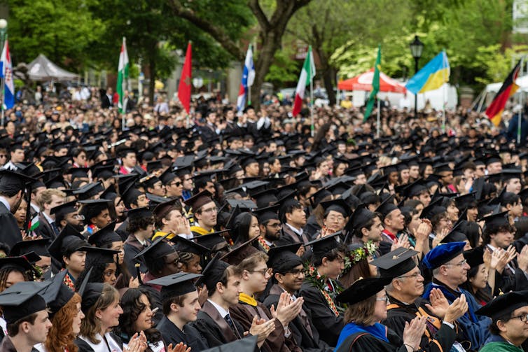 A large gathering of people seated at an outdoor ceremony and wearing graduation caps and gowns