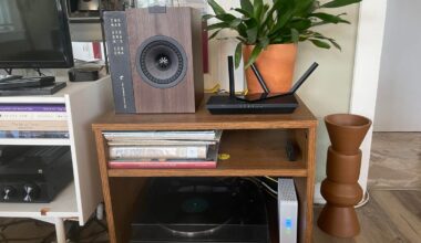 a black router on a side table in front of a potted plant and next to a speaker