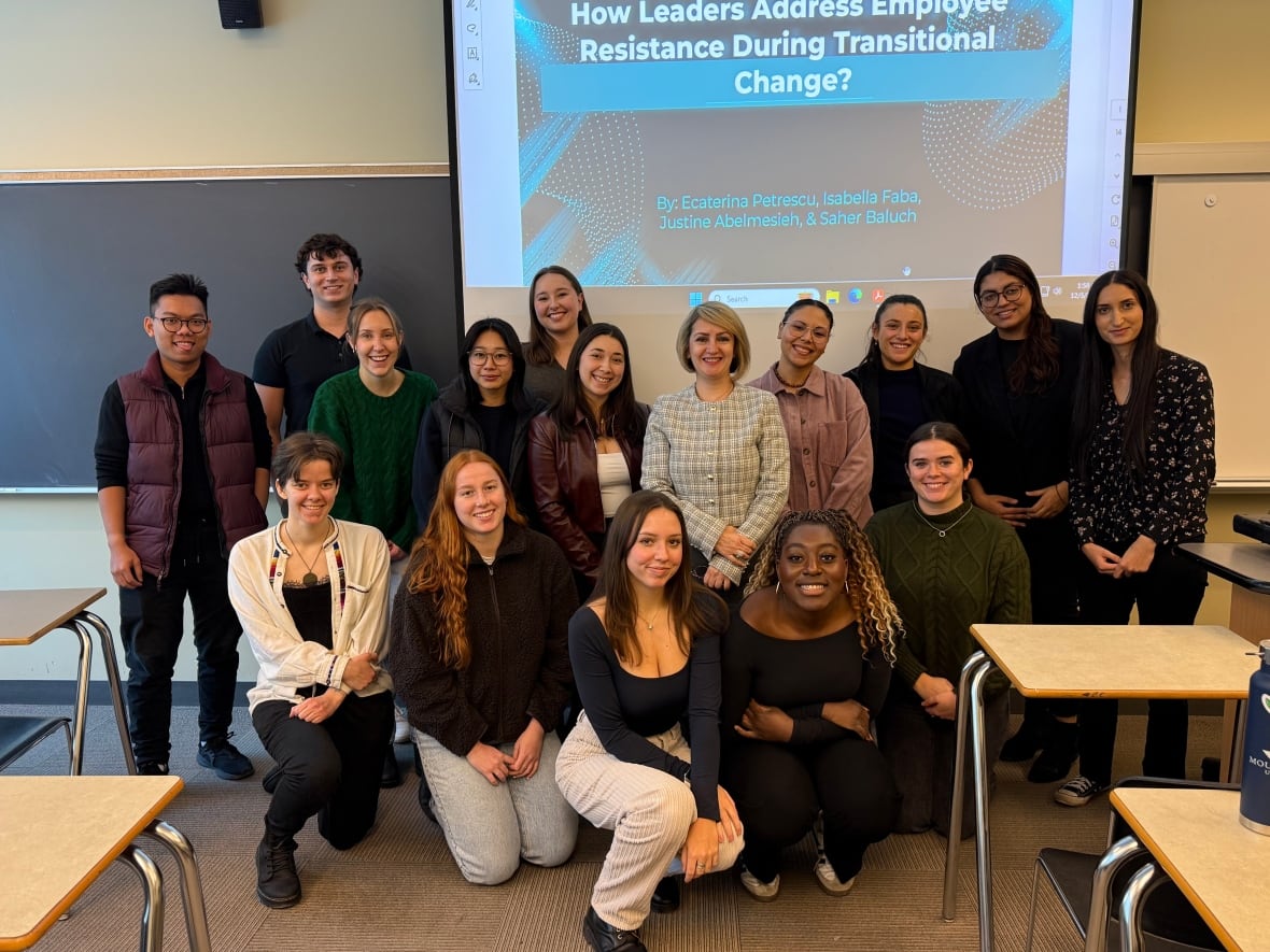 A group of students stands with their professor at the front of a classroom.