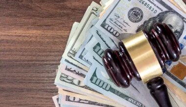 Wooden judge's gavel sitting on top of a spread of cash on a wooden surface