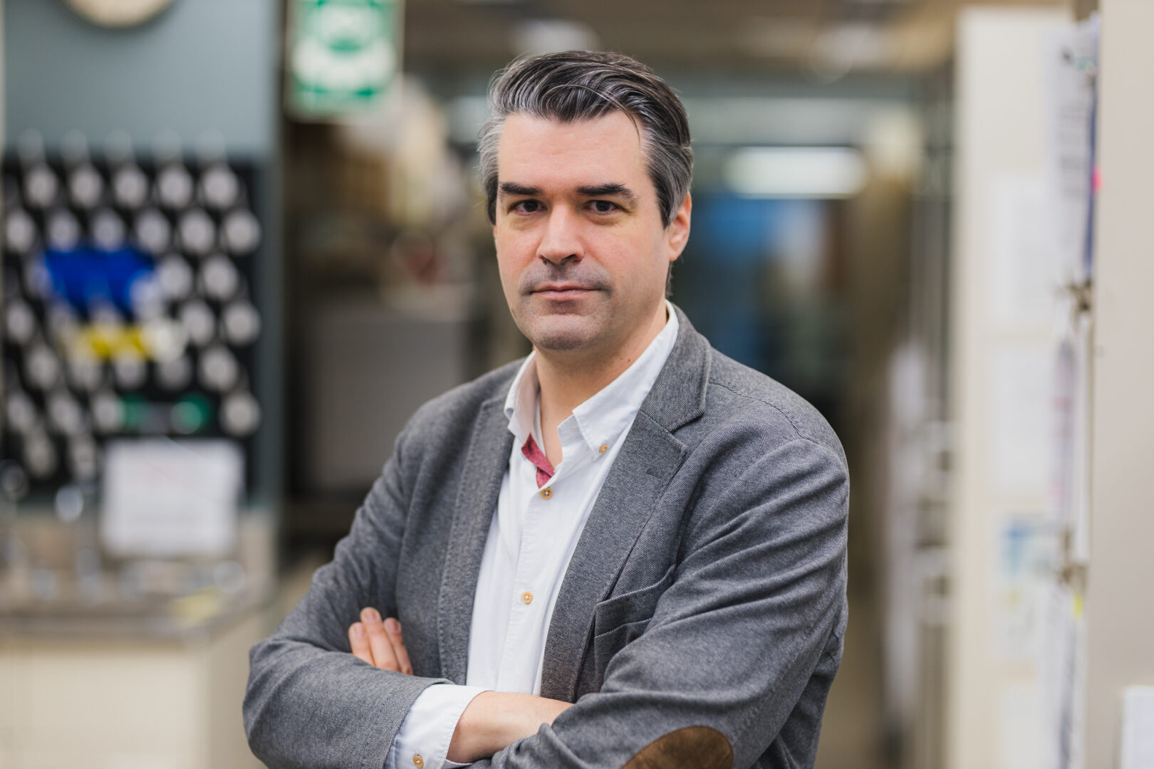 Head and shoulders photo of Dr. Dr. Guillaume Paré, with his arms crossed, smiling with his lab in the background.