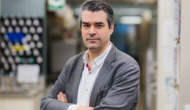 Head and shoulders photo of Dr. Dr. Guillaume Paré, with his arms crossed, smiling with his lab in the background.