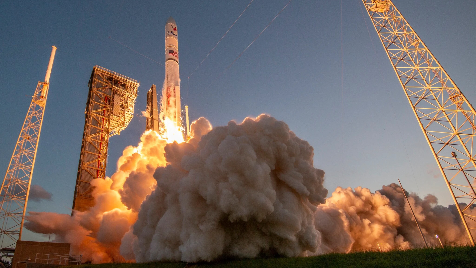 a white and red rocket launches into a blue sky, generating a huge plume of gray-white exhaust