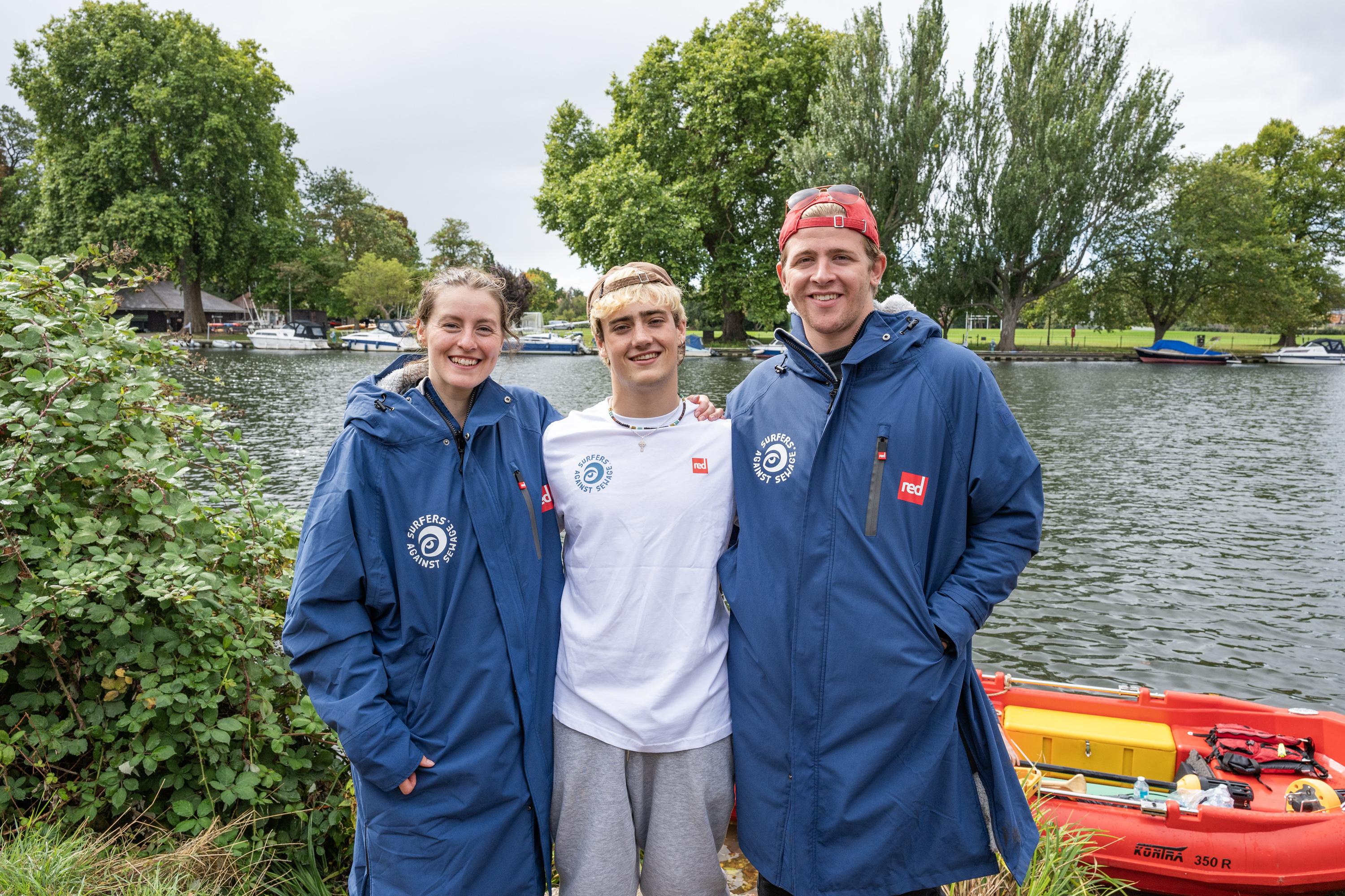 Three swimmers posing for a photo by a river, advocating for action against sewage pollution.