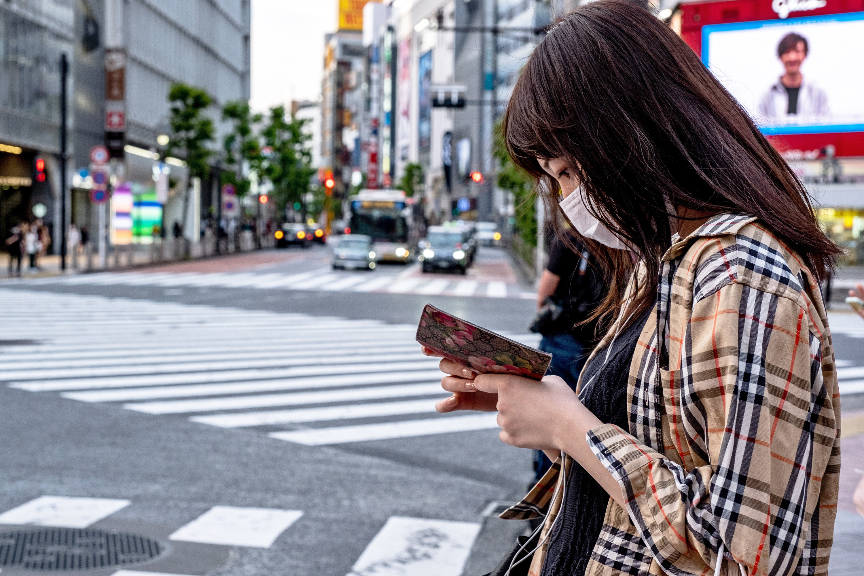 Woman wearing a face mask looks at her phone while waiting to cross a street in Shibuya, Tokyo.