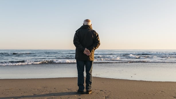 Retired older man strolling on the beach in winter. 