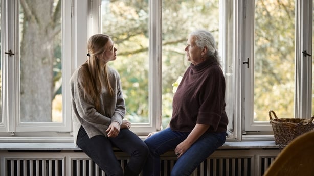 a grandmother and grand daughter sitting on a window sill talking