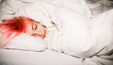 a pink haired teen's head is sleeping in a bundle of white sheets and blankets