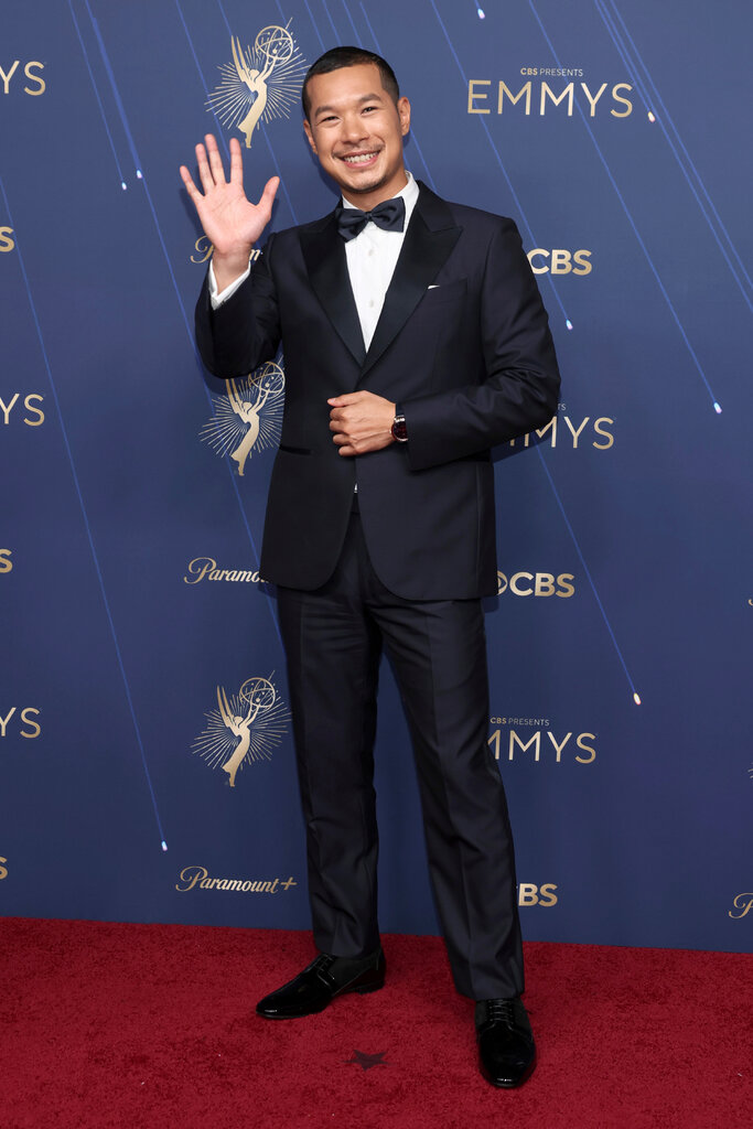 A man in a navy suit waves at the camera.