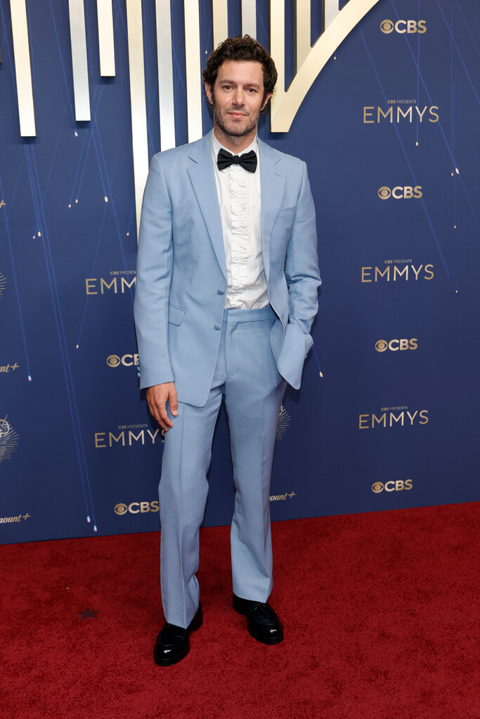 A man wears a blue suit with a ruffled white shirt.