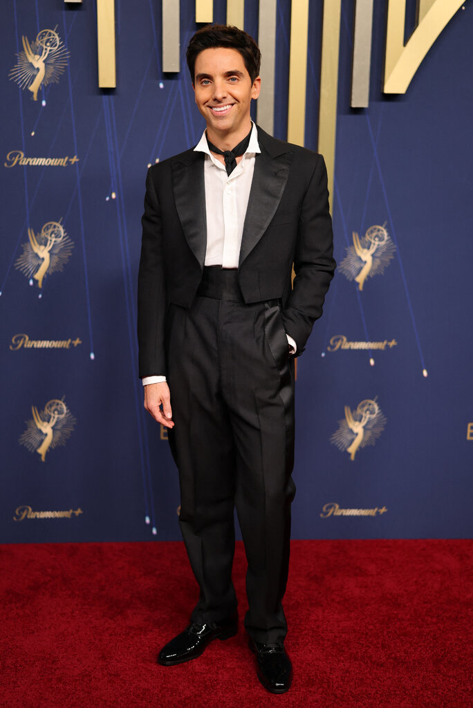 A man wearing a tuxedo and black ascot poses on the red carpet.