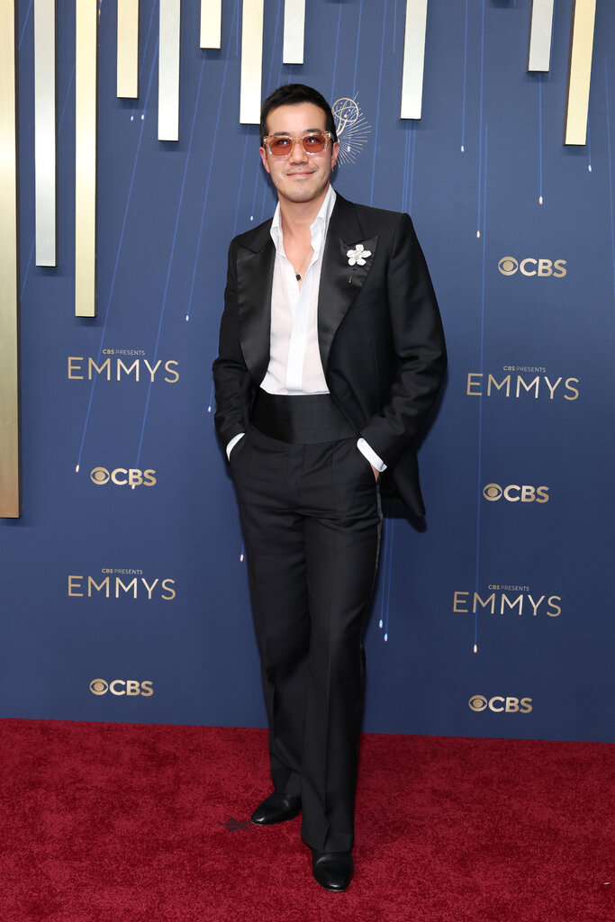 A man in a tuxedo and sunglasses poses with his hands in his pockets.