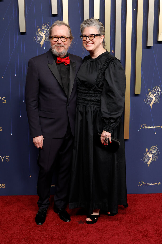 A man in a black suit and red bowtie (left) poses with a woman in a black dress.