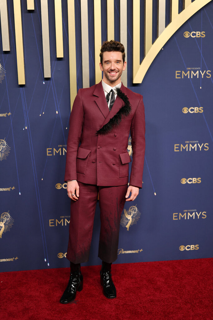 A man wears a maroon suit with a feather at the lapel.