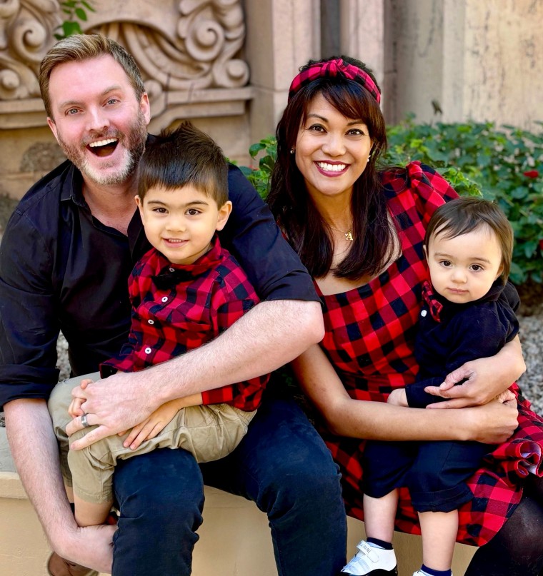 A man and his wife sit on a stoop holding their two young children.
