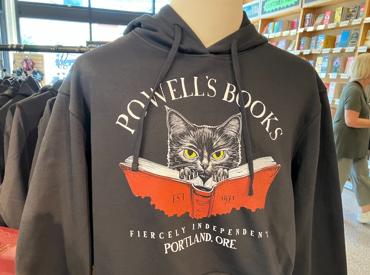 A drawing of a cat with its claws digging into the top of a book is depicted on a black sweatshirt.
