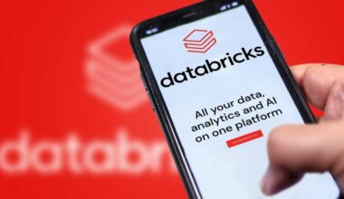 A photograph of a Databricks website on a phone being held in front of a larger, blurry version of the Databricks logo.