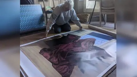 BBC/Jo Burn Deidre Kashdan kneeling on the floor of her studio, she is laying out a piece of artwork which is inspired by the Victorian era trend of "Hidden Mother" photography.
