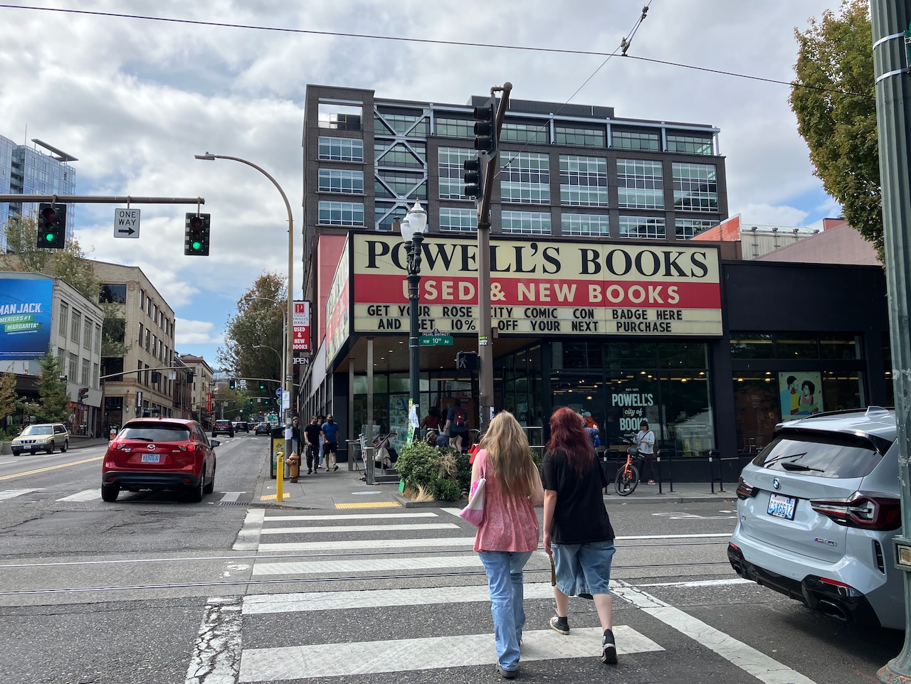 Two pedestrians cross in a crosswalk toward the front doors of Powell's Books.