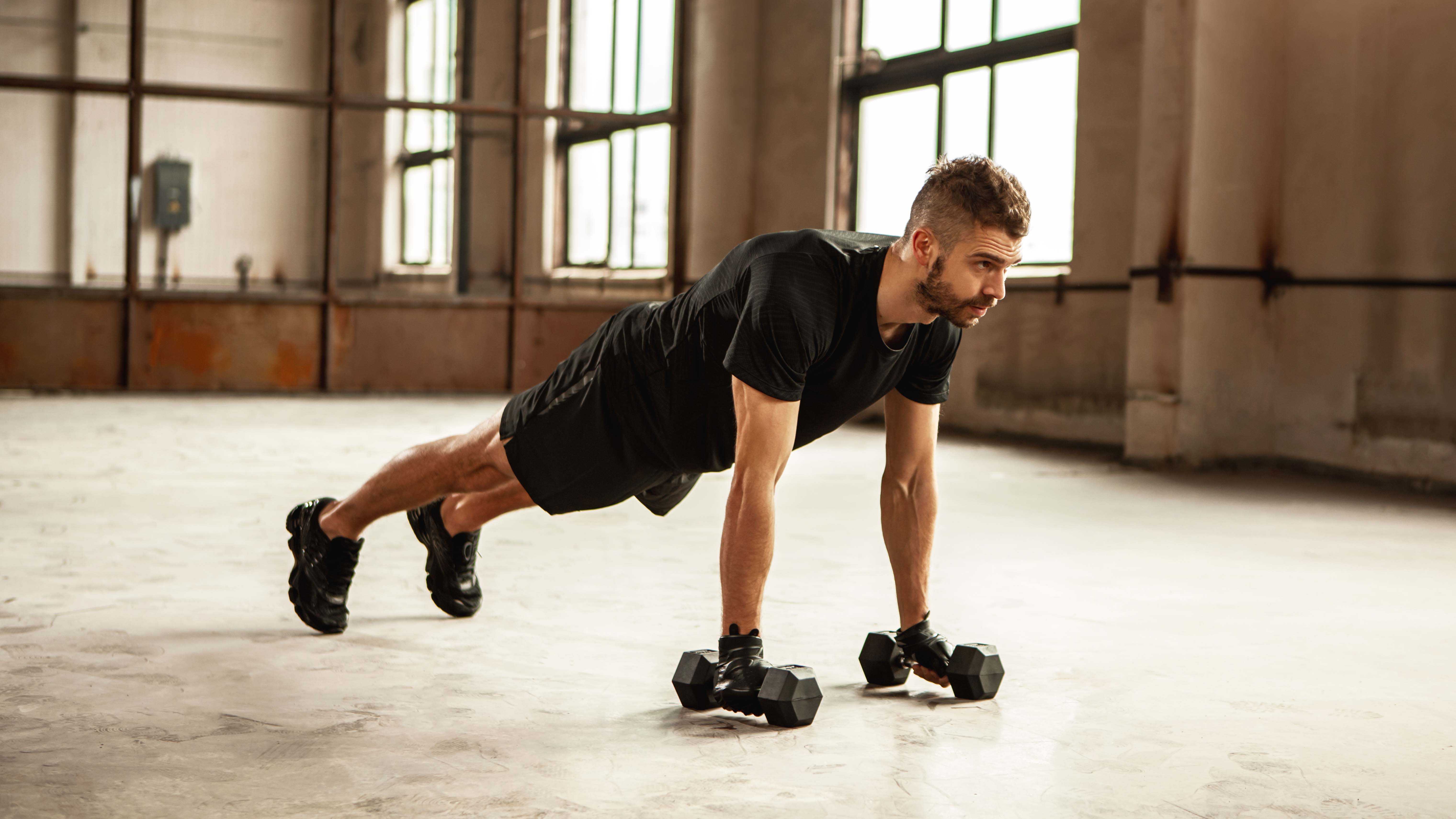 a photo of a man in a high plank with a dumbbell in both hands