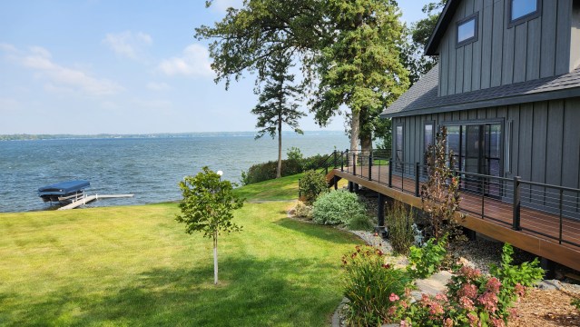 The side of a grey house along a swath of bright green lawn facing an open body of water.