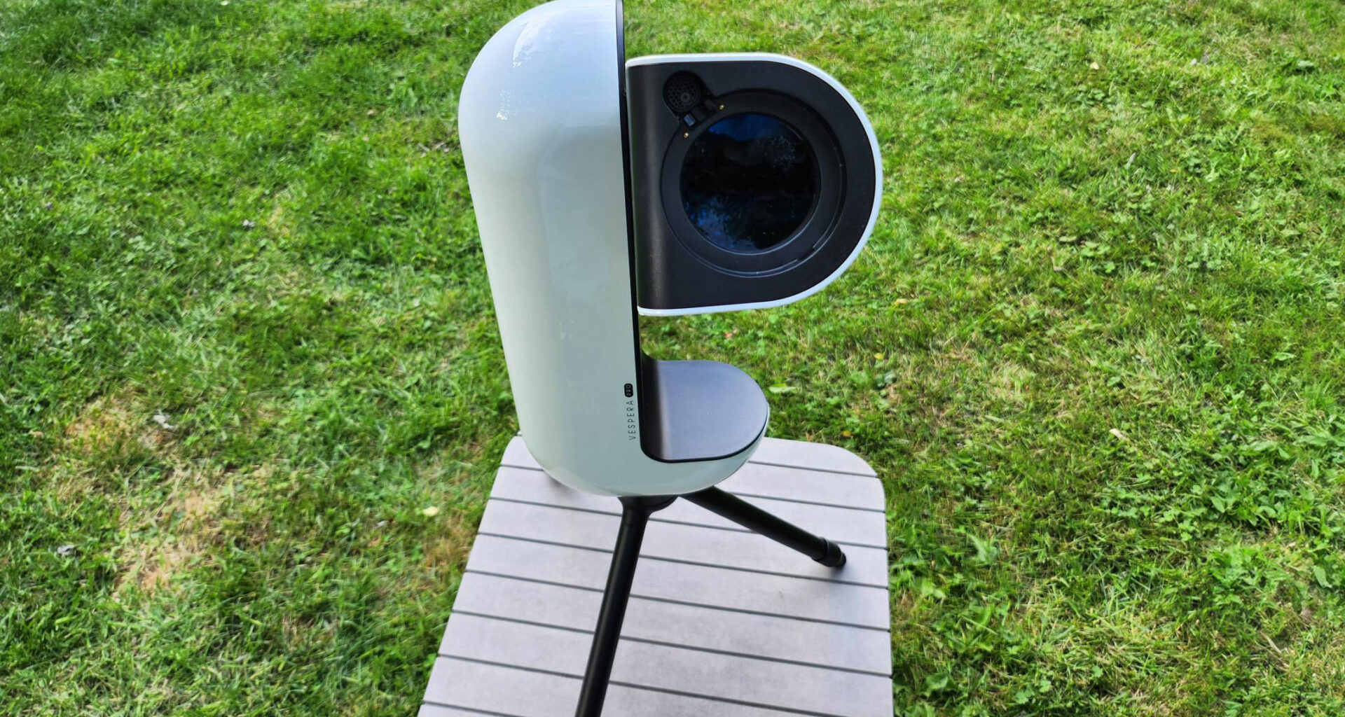 The Vaonis Vespera Pro smart telescope pointing at the sky on a brown table with grass in the background.