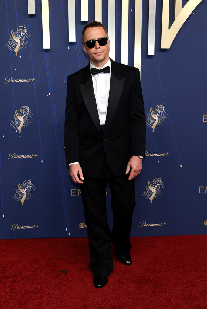 A man wears a black suit and sunglasses.