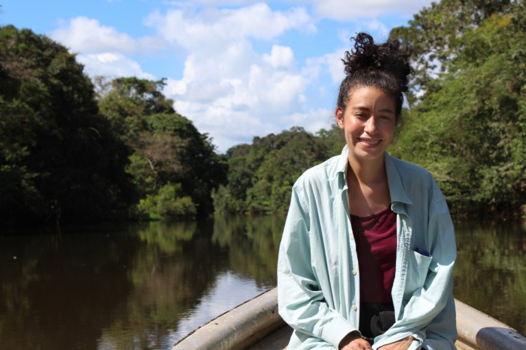 Valeria Ramírez Castañeda, wearing a lab jacket, sat in a boat on a forested waterway.