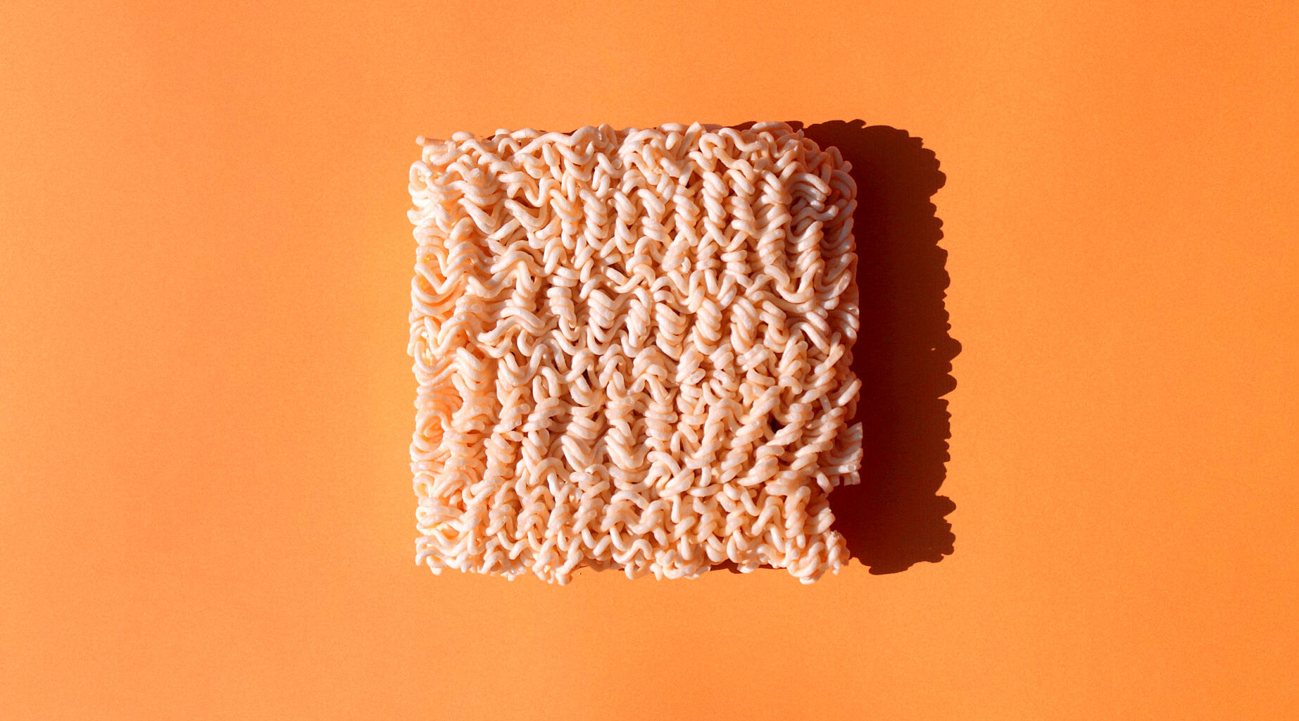 a brick of uncooked ramen noodles sits on an orange background