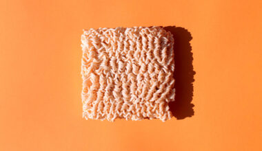 a brick of uncooked ramen noodles sits on an orange background