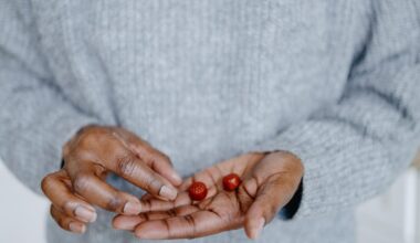 A close up of a person's hand holding two red gummy supplements. They are wearing a light grey sweater.