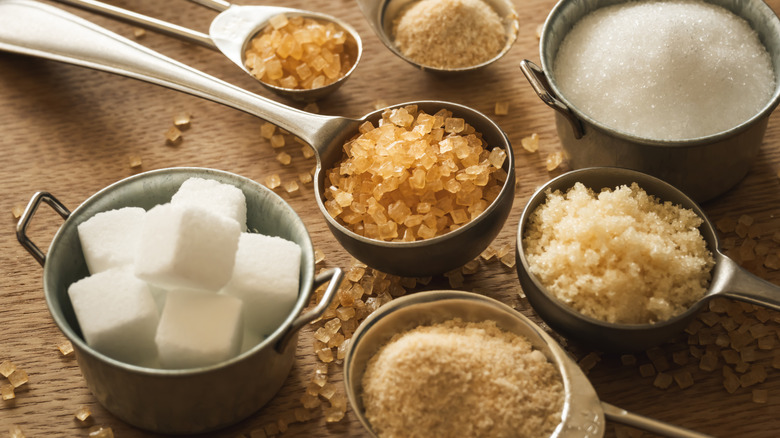 Measuring cups and spoons filled with sugar cubs, granulated sugar, sugar in the raw, and brown sugar