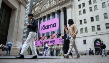 Large pink Klarna signs displayed on the New York Stock Exchange building as people walk by during Klarna's IPO.