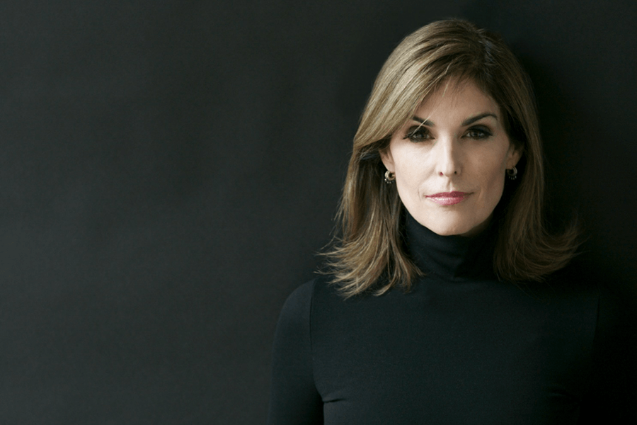 A headshot of a woman staring at the camera with a slight smile, wearing a black turtleneck against a dark background.