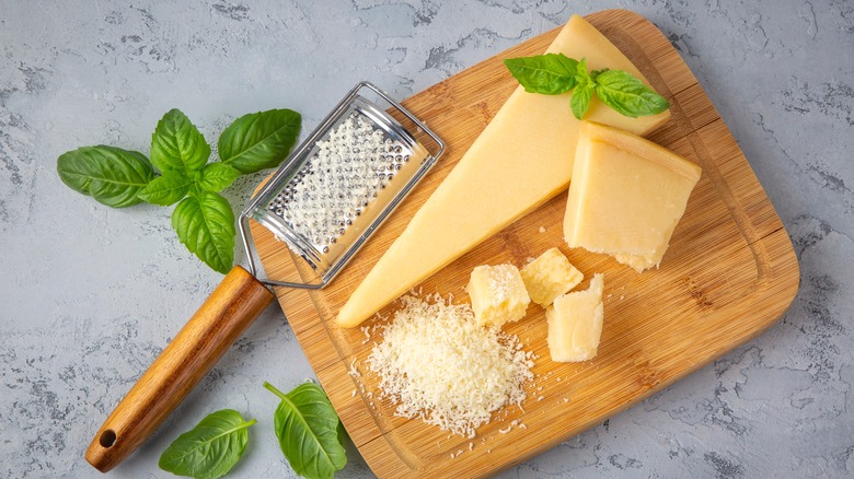 Hard parmesan cheese, partially grated on a cutting board