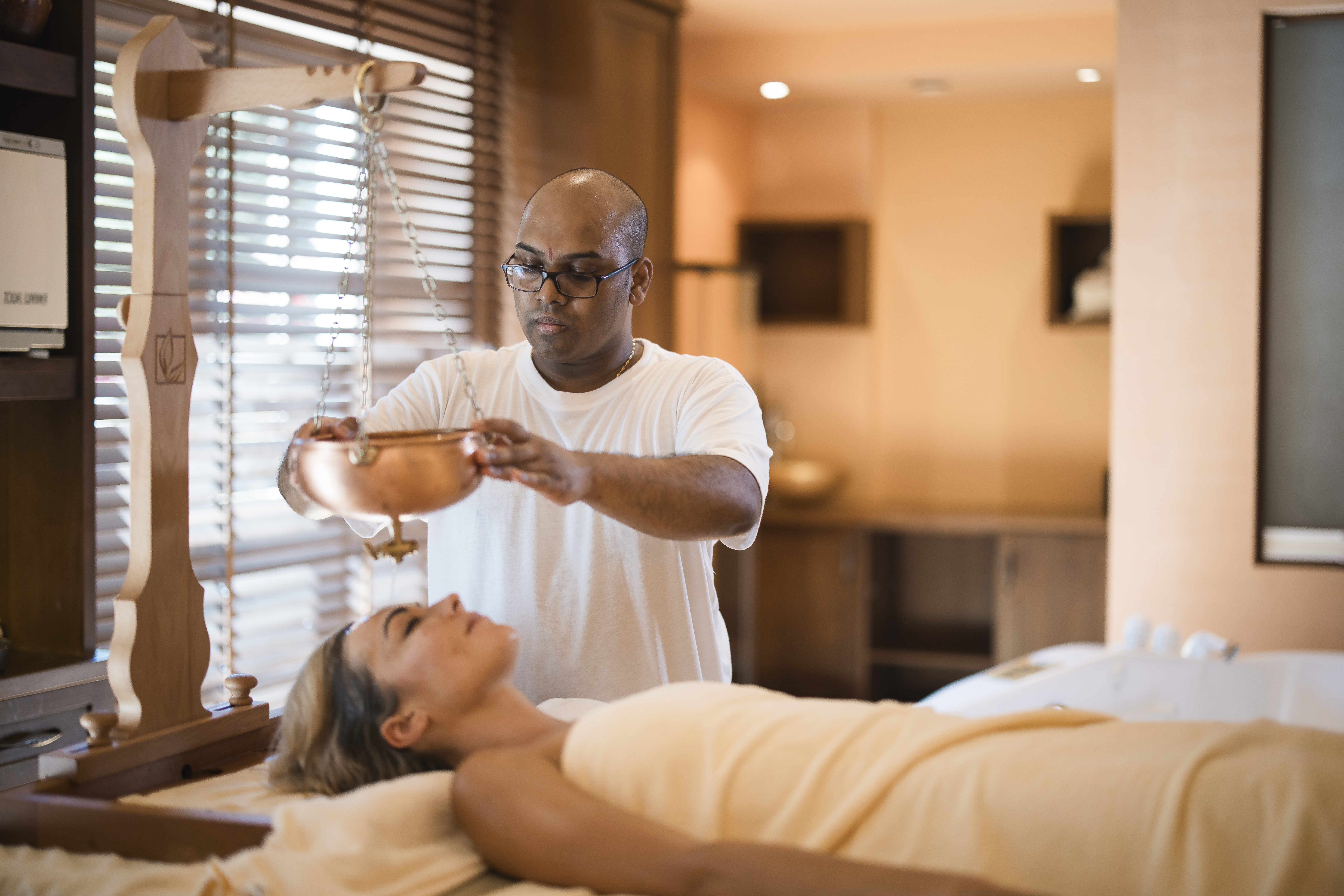 Man performing a traditional Ayurvedic shirodhara treatment on a woman.