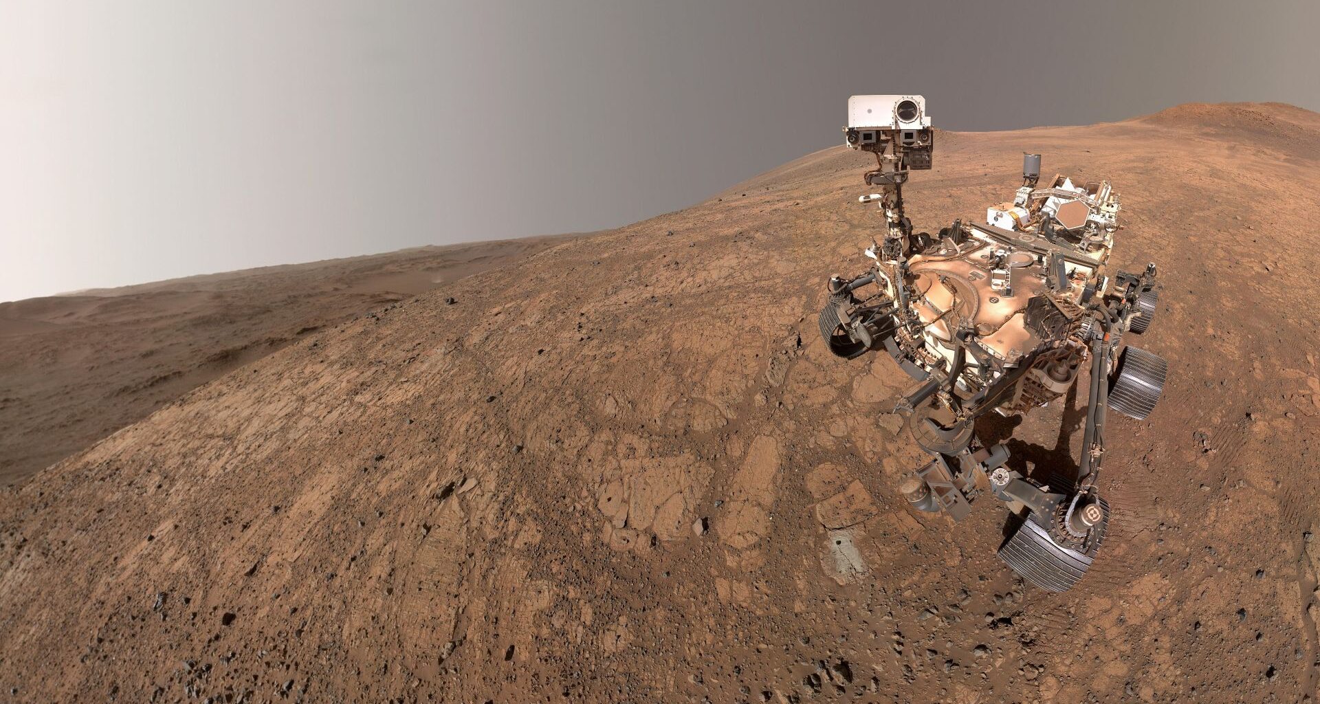 A rover sits on the reddish brownish surface of Mars