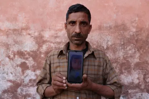 Reuters Govind Ram shows a picture, on his phone, of his daughter Surbhi Sharma, 3, who along with other children died due to kidney injury after consuming contaminated cough syrup in Jammu between December 2019 and January 2020, near a park in Ramnagar on the outskirts of Jammu, India, March 28, 2023. REUTERS/Anushree Fadnavis