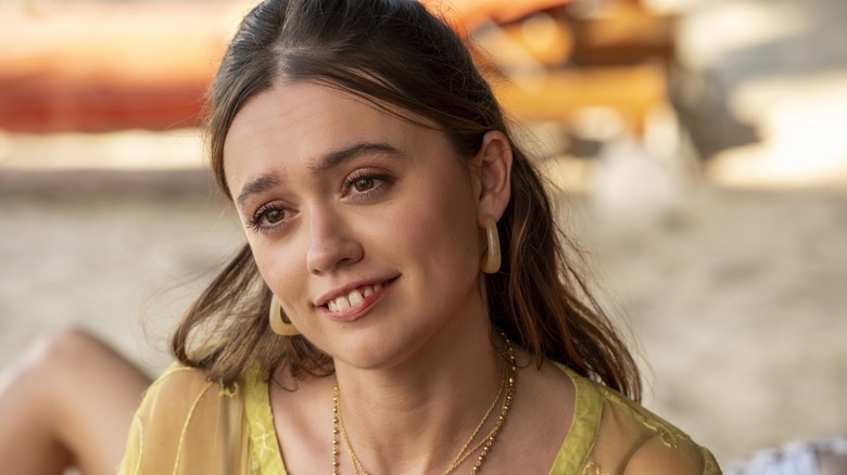 Aimee Lou Wood as Chelsea, sitting on the beach and smiling on The White Lotus