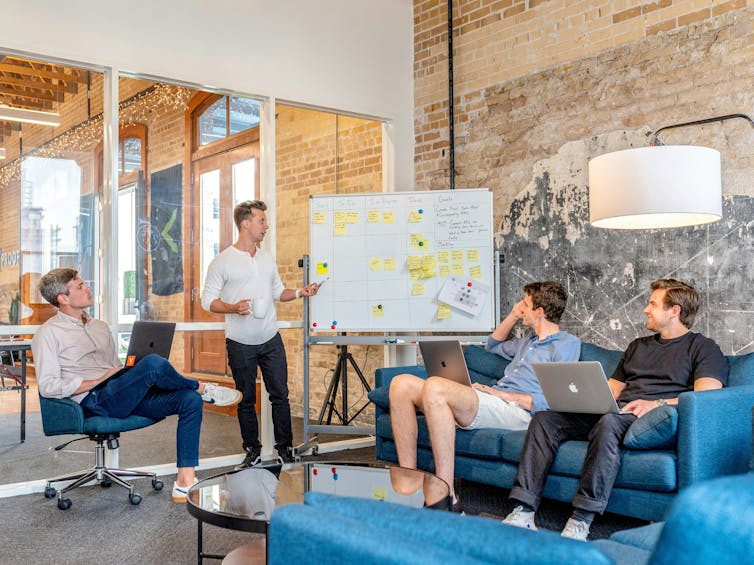A group of people sitting around a whiteboard, having a discussion