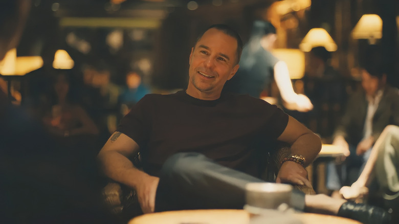 Sam Rockwell as Frank, sitting in a chair and smiling in The White Lotus